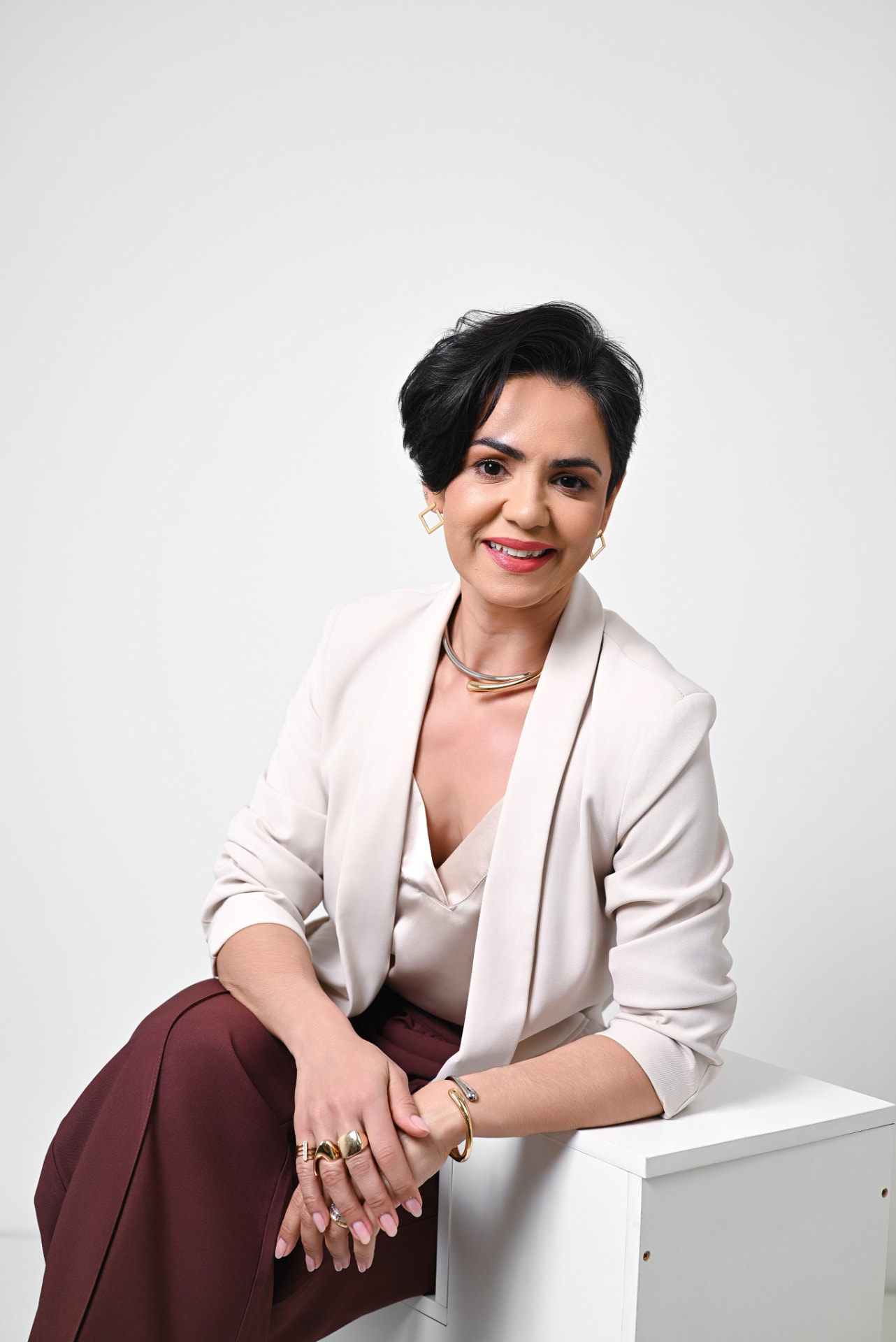 Fabi Souza sentada, sorrindo, com blazer bege